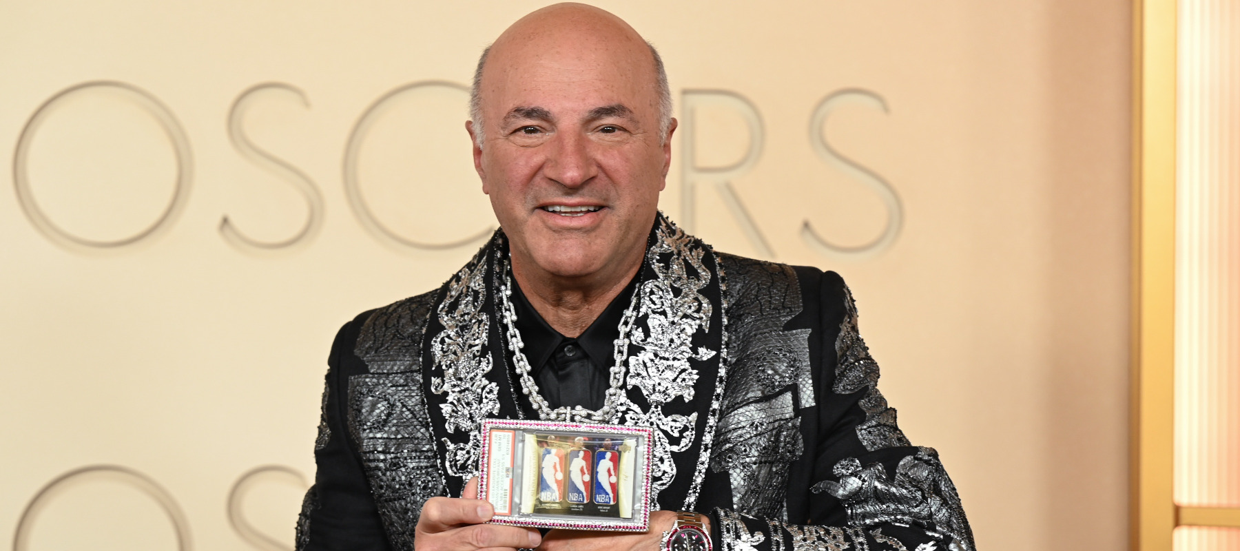 Kevin O'Leary holding a gold and diamond chain with a display case showcasing NBA trading cards