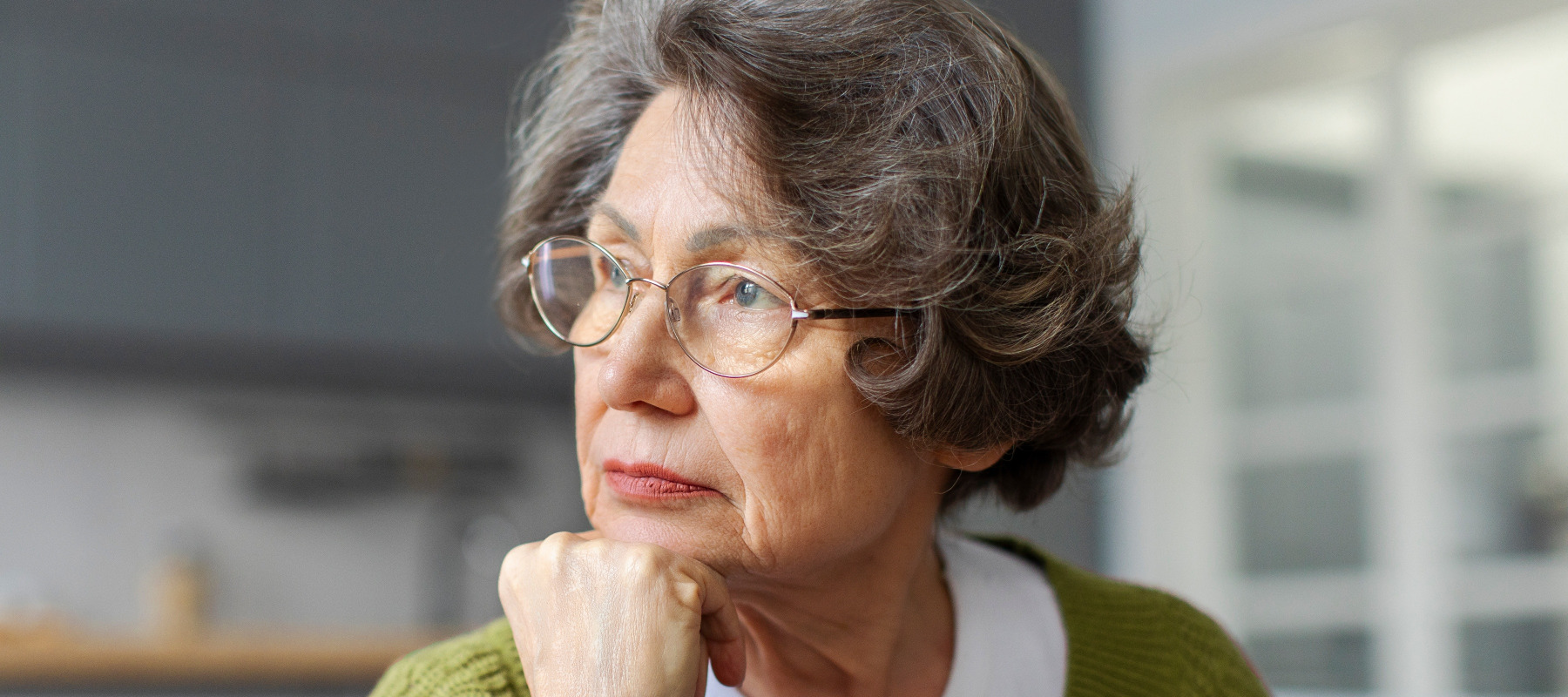 Pensive senior woman resting on sofa at home looking out window.