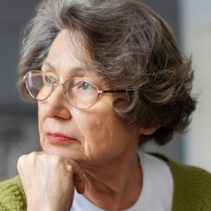 Pensive senior woman resting on sofa at home looking out window.
