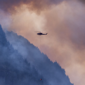 Wildfire Service Helicopter flying over BC Forest Fire and Smoke on the mountain near Hope during a hot sunny summer day
