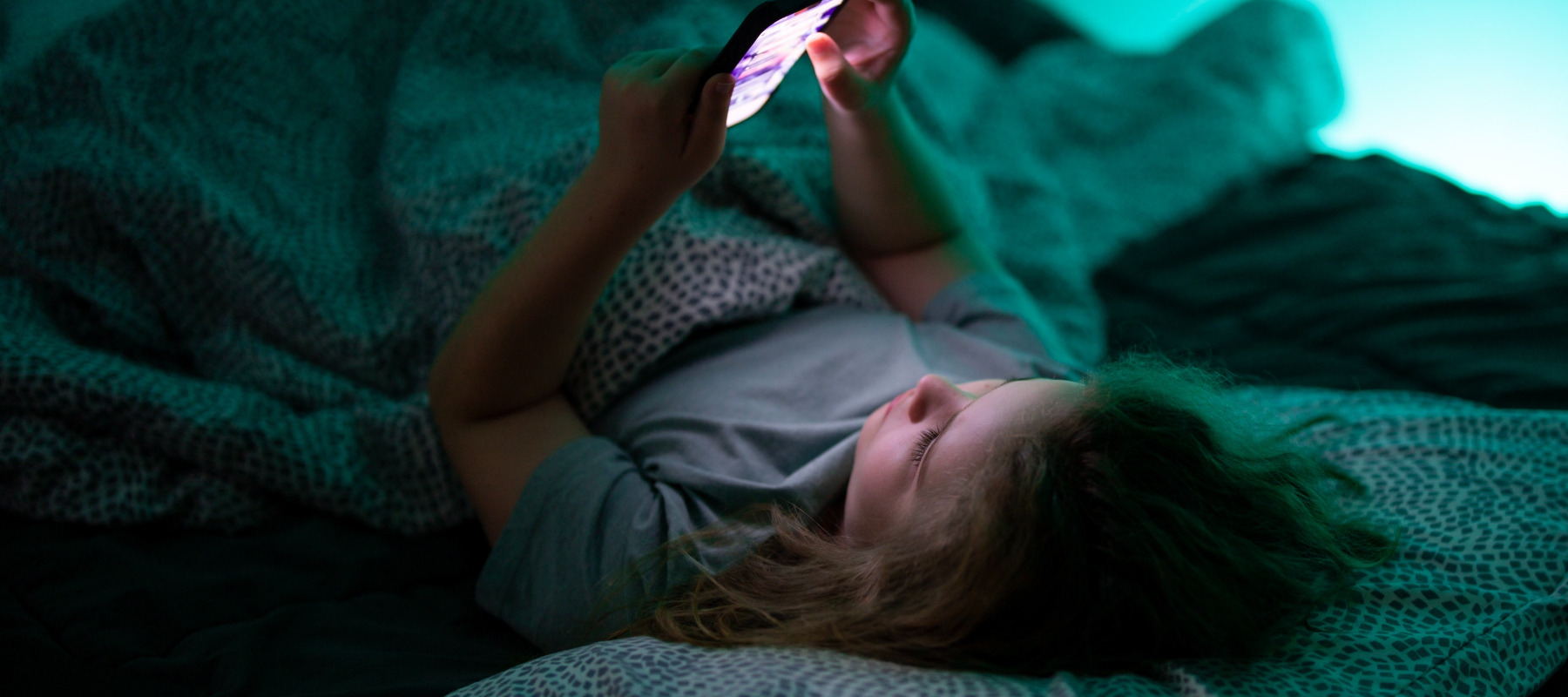 Child on cell phone in bed at night