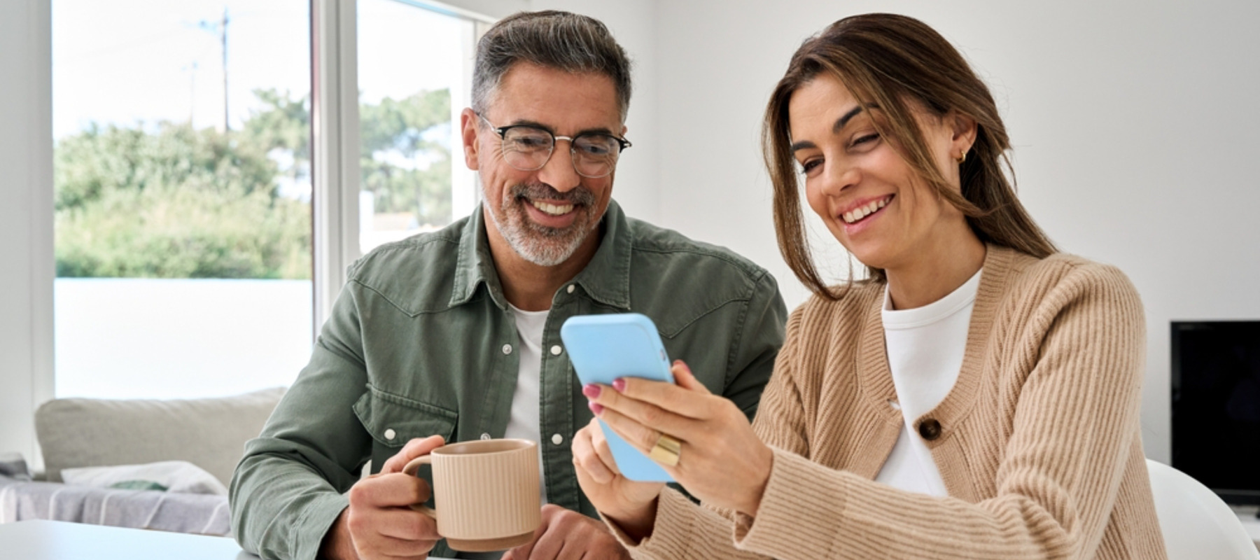 Middle aged happy couple using smartphone relaxing at living room table at home