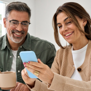 Middle aged happy couple using smartphone relaxing at living room table at home