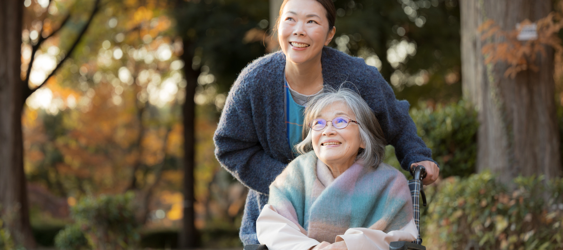 Older daughter pushing her elderly mother in a wheelchair on an outdoor path