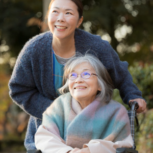 Older daughter pushing her elderly mother in a wheelchair on an outdoor path