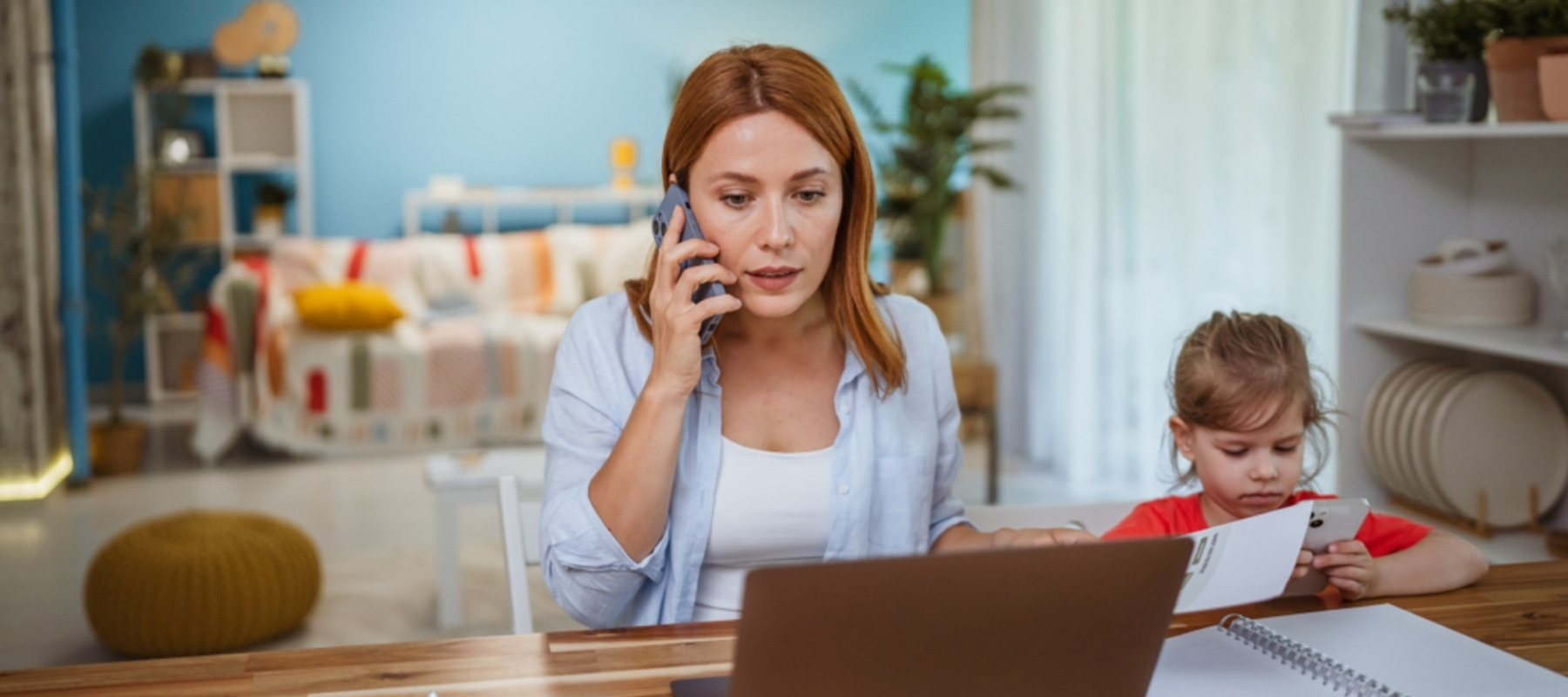 Young mother on the phone looking worried in front of her laptop with her daughter by her side
