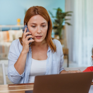 Young mother on the phone looking worried in front of her laptop with her daughter by her side