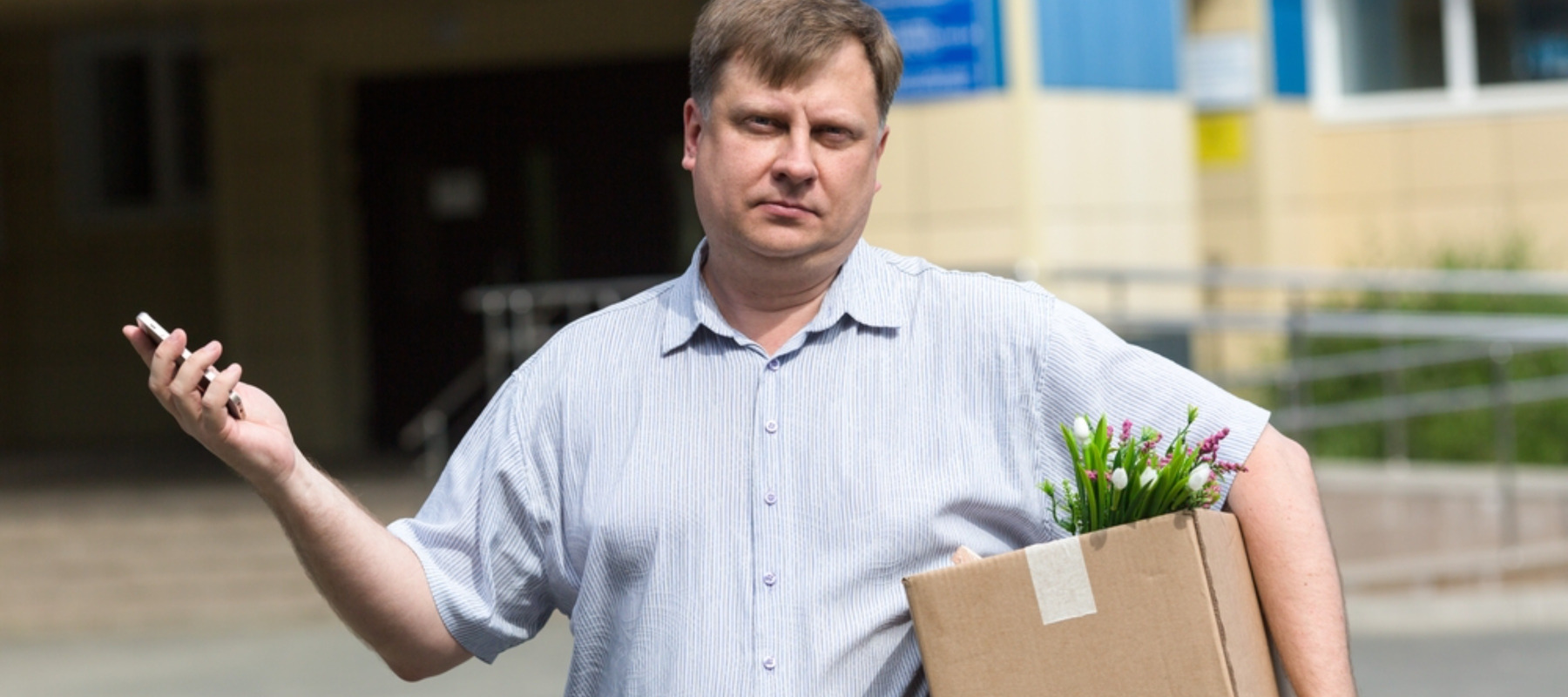 An adult man with a box of personal belongings calls on the phone about getting a new job