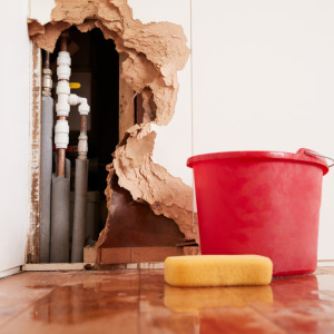 Retired couple having fun on vacation + damaged wall, exposed burst water pipes, sponge and bucket