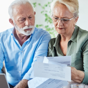 Senior couple checking bills and calculating expenses using a laptop at home,