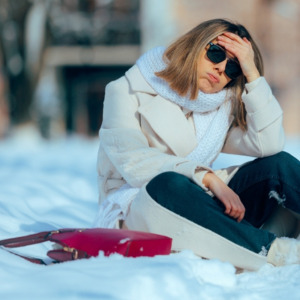 Frustrated woman sits down after shovelling snow