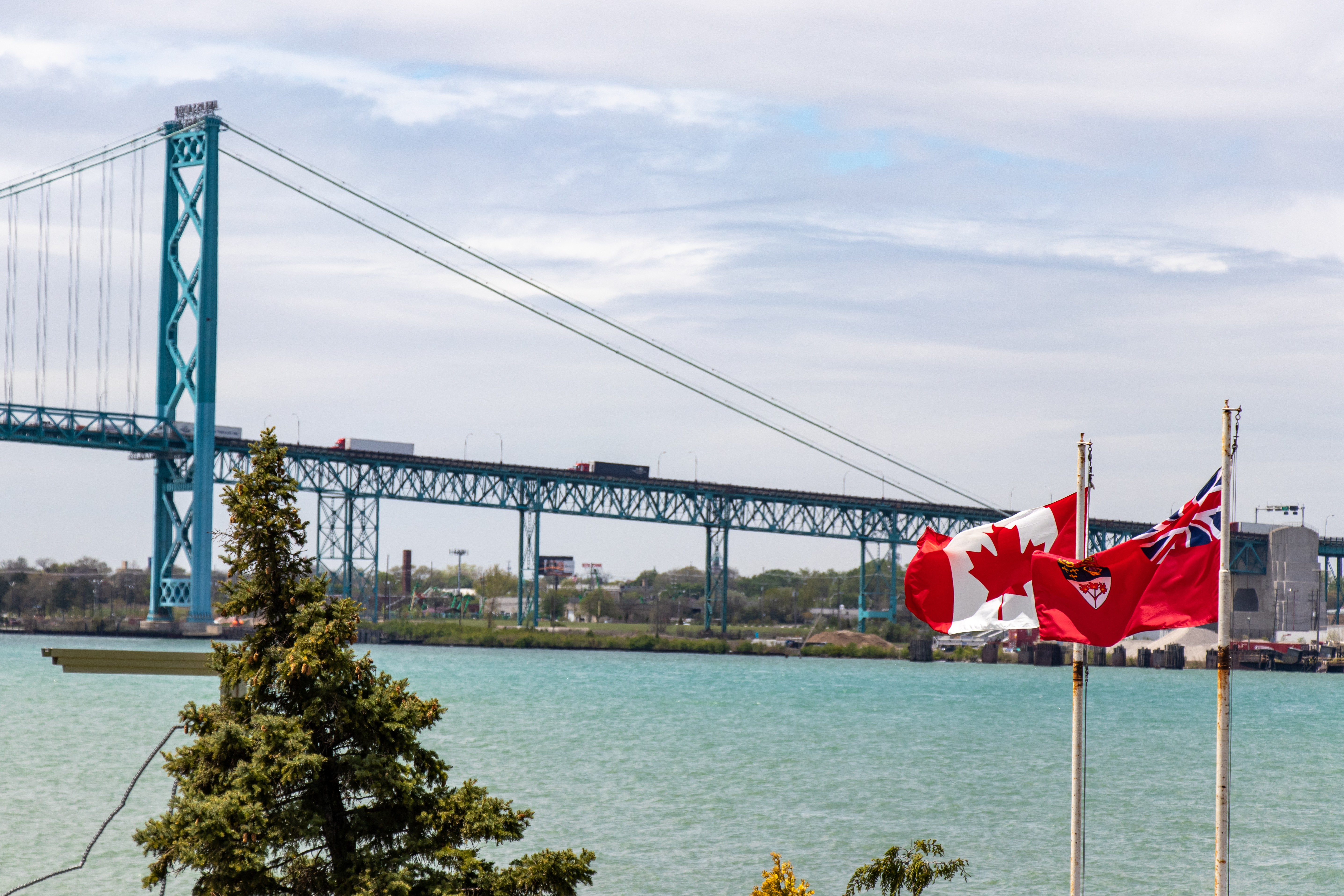 Windsor, Canada - May 21, 2020: Canada and Ontario flags seen waving in-front of the the US-Canada border, Ambassador Bridge crossing on sunny day.